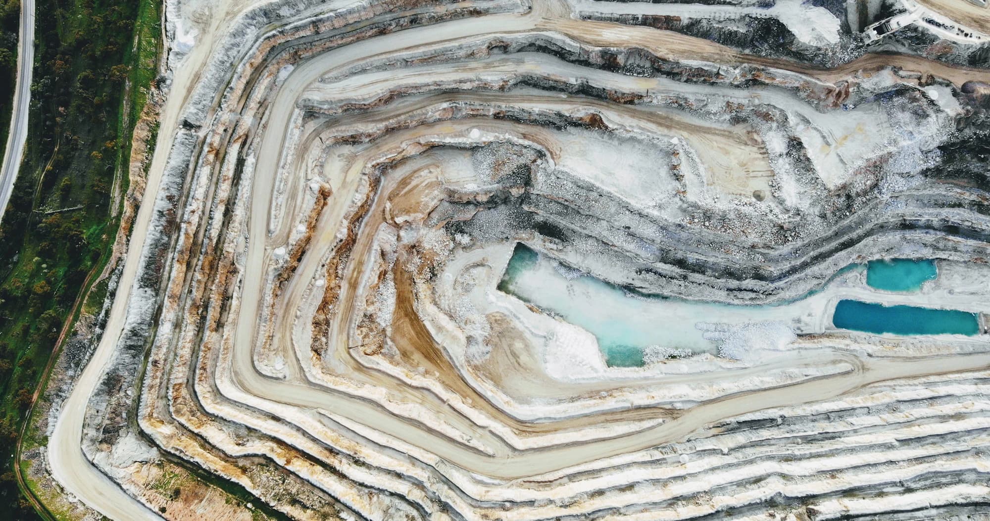 Aerial view of a terraced open-pit quarry, with haul roads along the benches and water pooled at the bottom