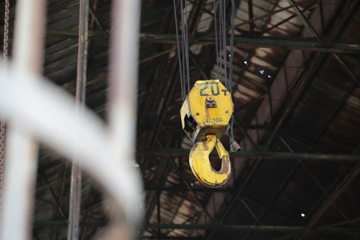 A yellow overhead crane hook hanging in an industrial building
